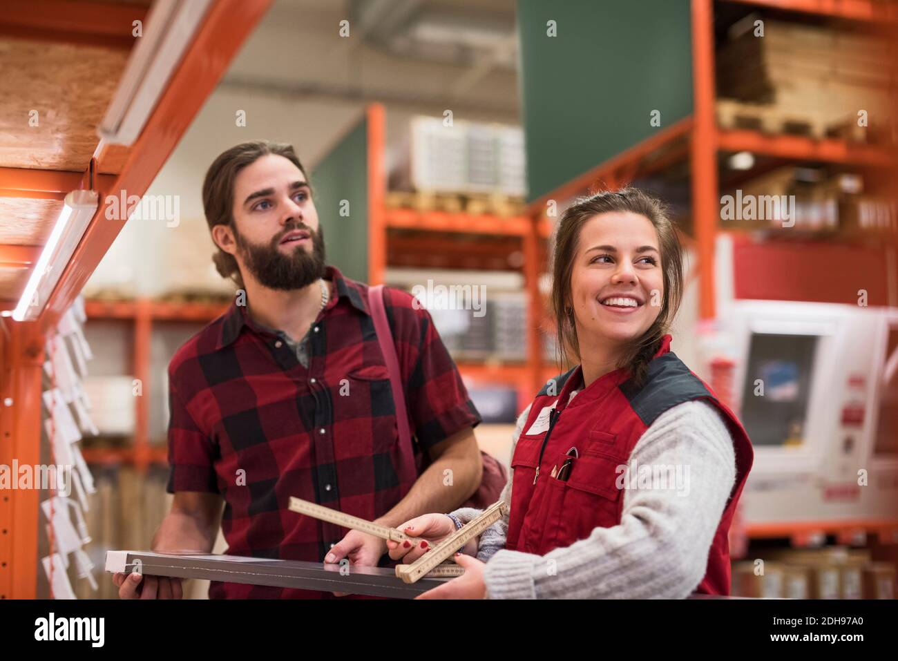 Happy saleswoman looking away while standing with male customer in hardware store Stock Photo