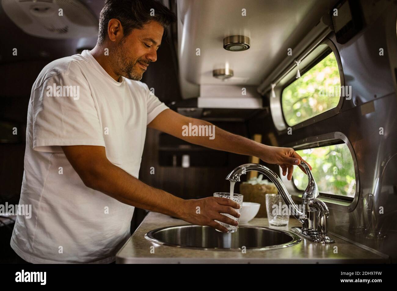 Smiling man filling drinking water through faucet in camper trailer Stock Photo