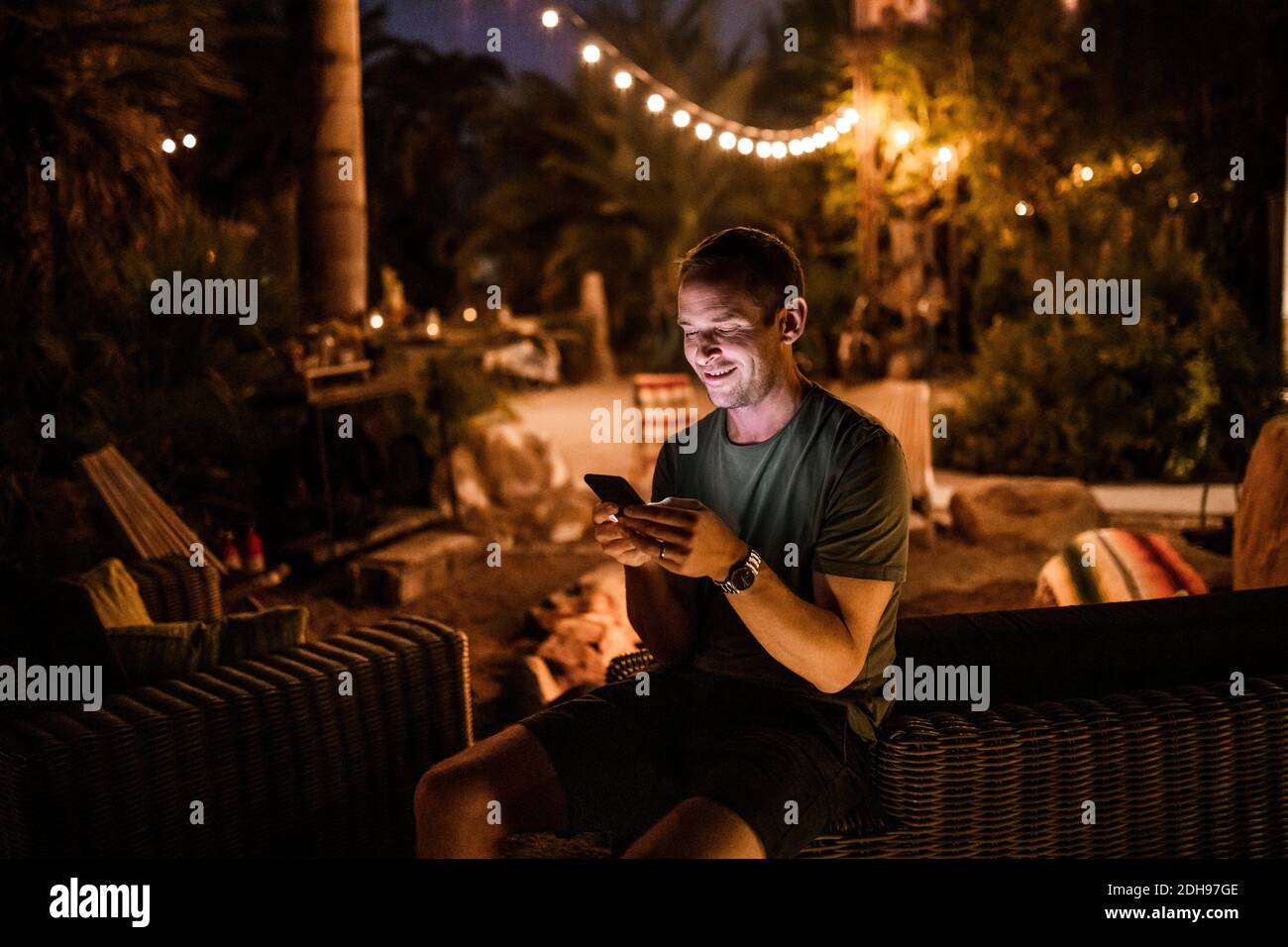 Smiling man using smart phone while sitting in garden during sunset Stock Photo