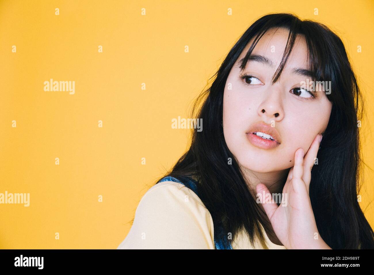 Close-up of girl looking away with hand on chin against yellow background Stock Photo