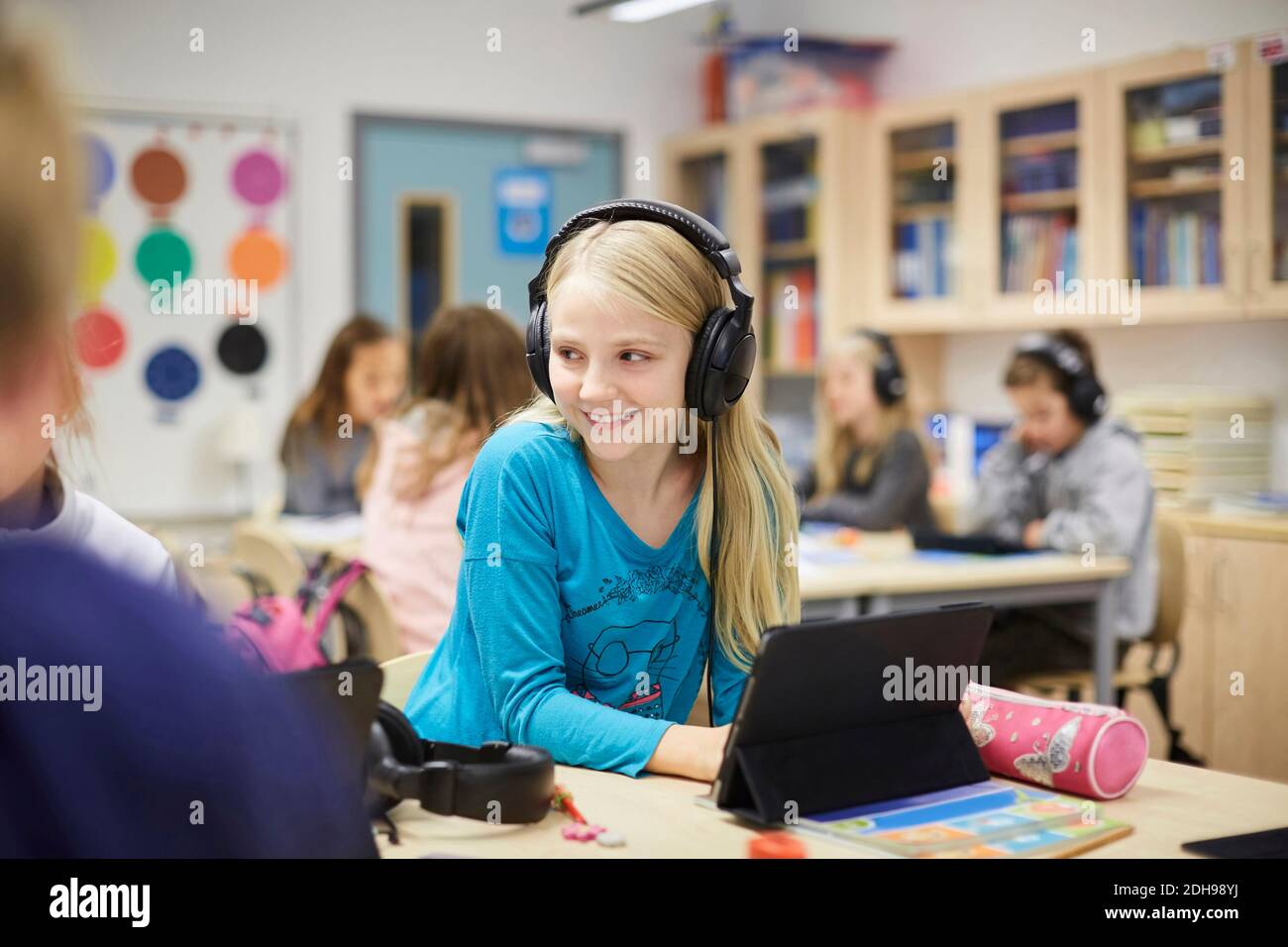 Smiling girl wearing headphones while using digital table in classroom Stock Photo