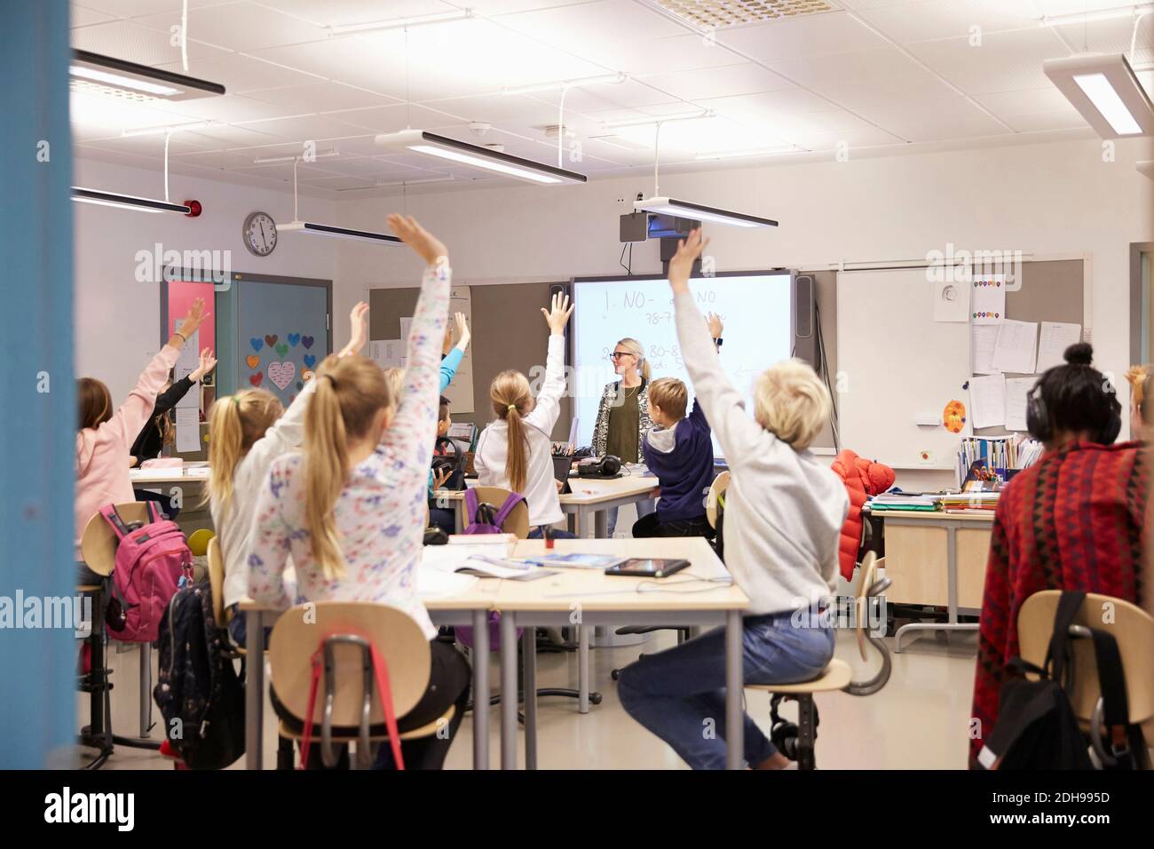 Teacher looking at students with arms raised in classroom Stock Photo