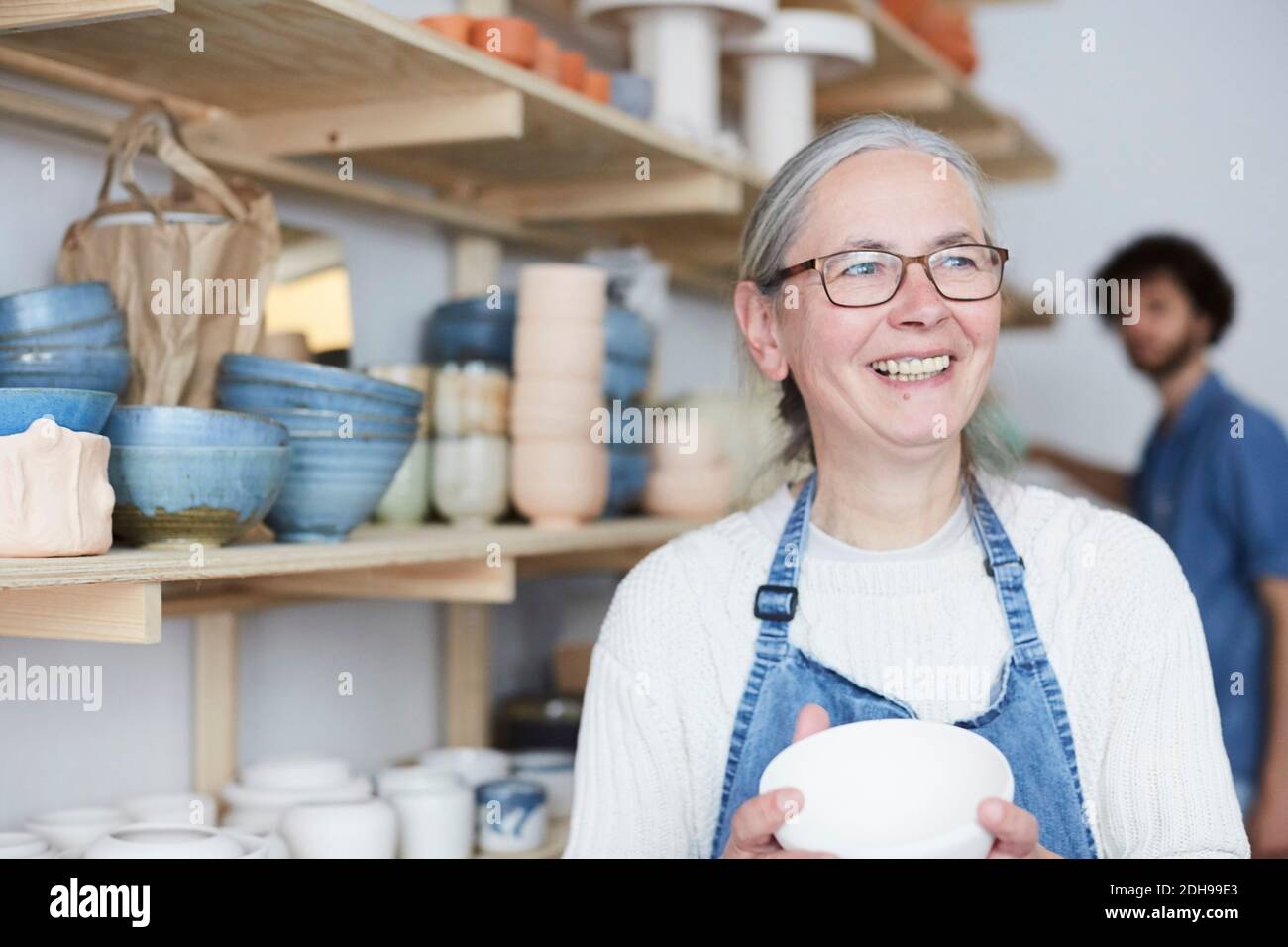 Smiling mature woman looking away while holding bowl in pottery class Stock Photo