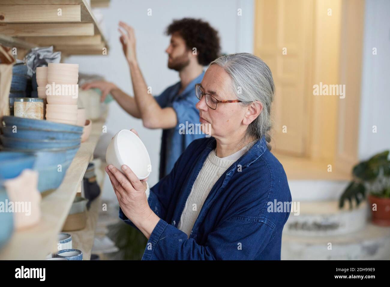 Man and woman arranging earthenware on shelf in art class Stock Photo