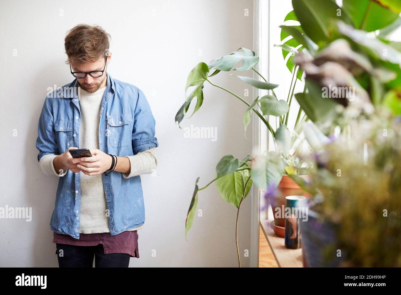 Young man using mobile phone against wall in art studio Stock Photo