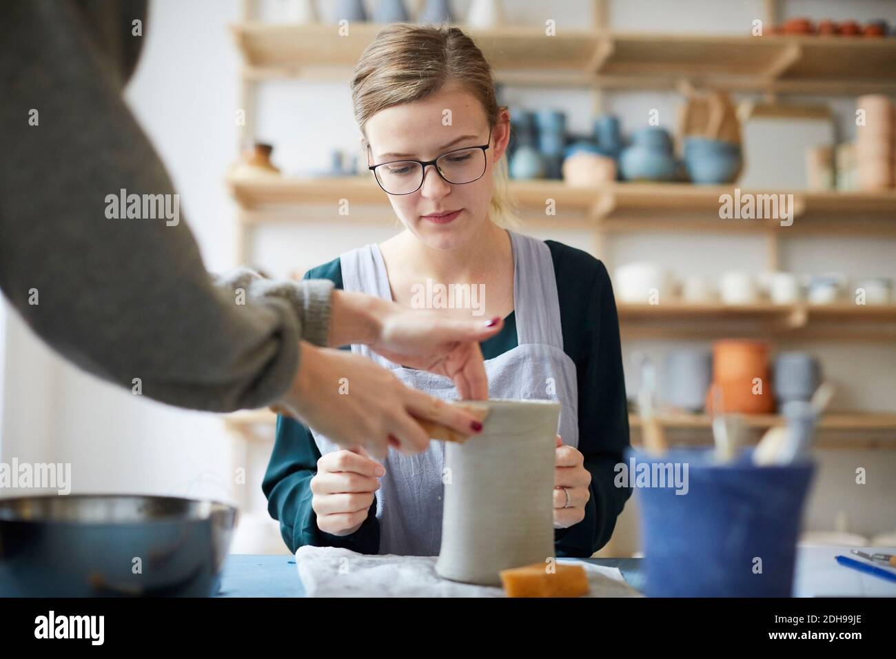 Female teacher assisting young woman in making pot in art class Stock Photo