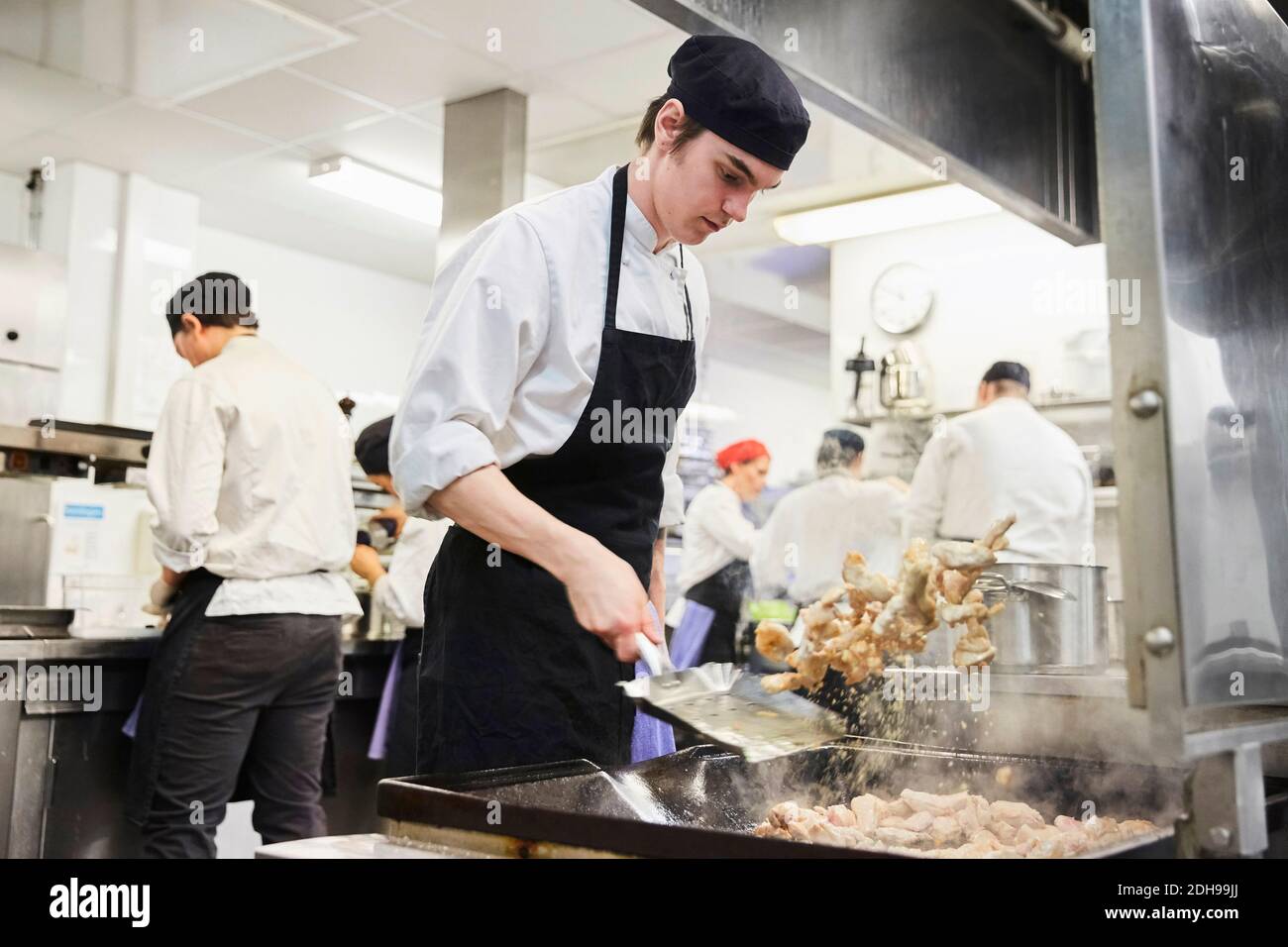 Male chef student tossing food with teacher and colleagues in background at cooking school Stock Photo