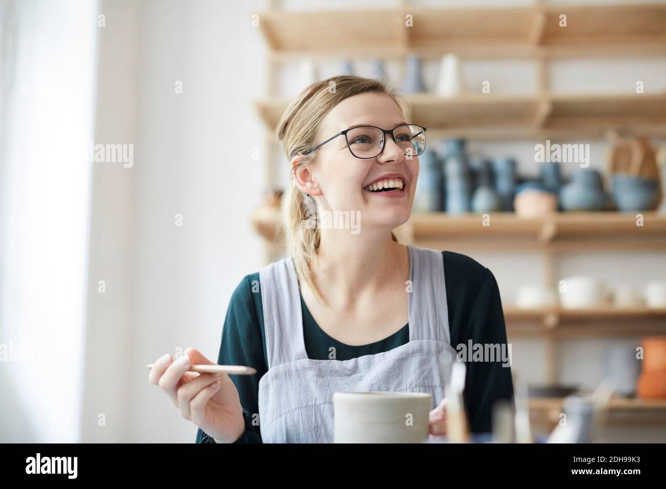 Smiling young woman looking up while learning pottery in art studio Stock Photo