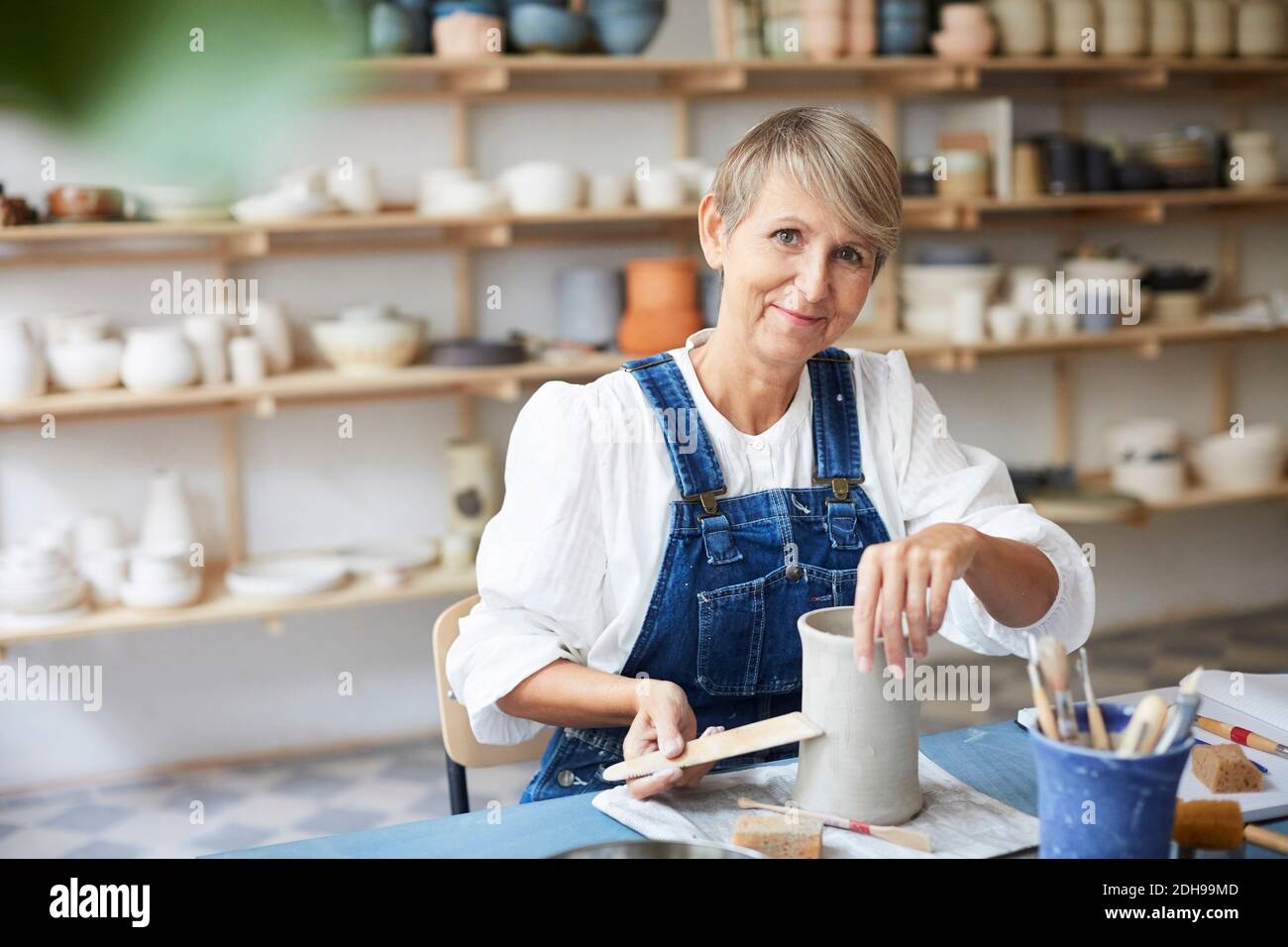 Portrait of smiling mature woman with earthenware at table in art studio Stock Photo