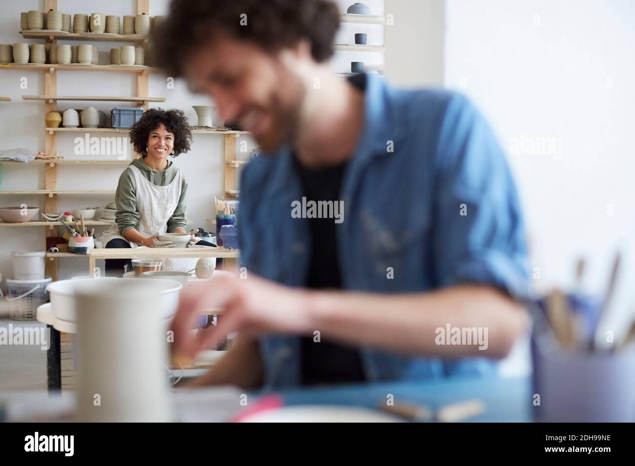 Portrait of smiling woman learning pottery while man in foreground at art studio Stock Photo