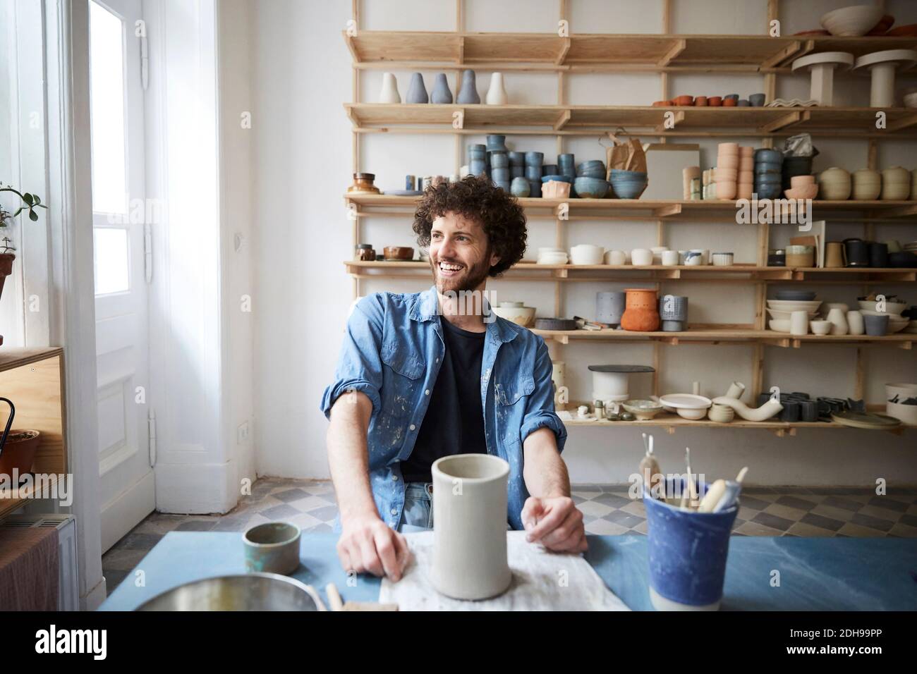 Smiling mid adult man looking away while sitting in pottery class Stock Photo