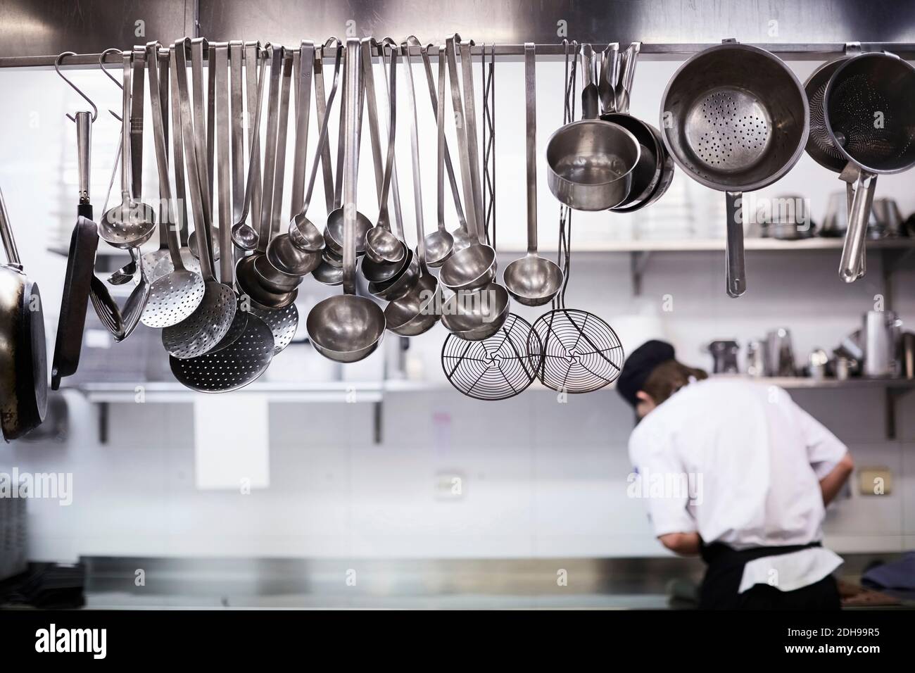 Utensils on metal rack with chef cooking in background at commercial kitchen Stock Photo