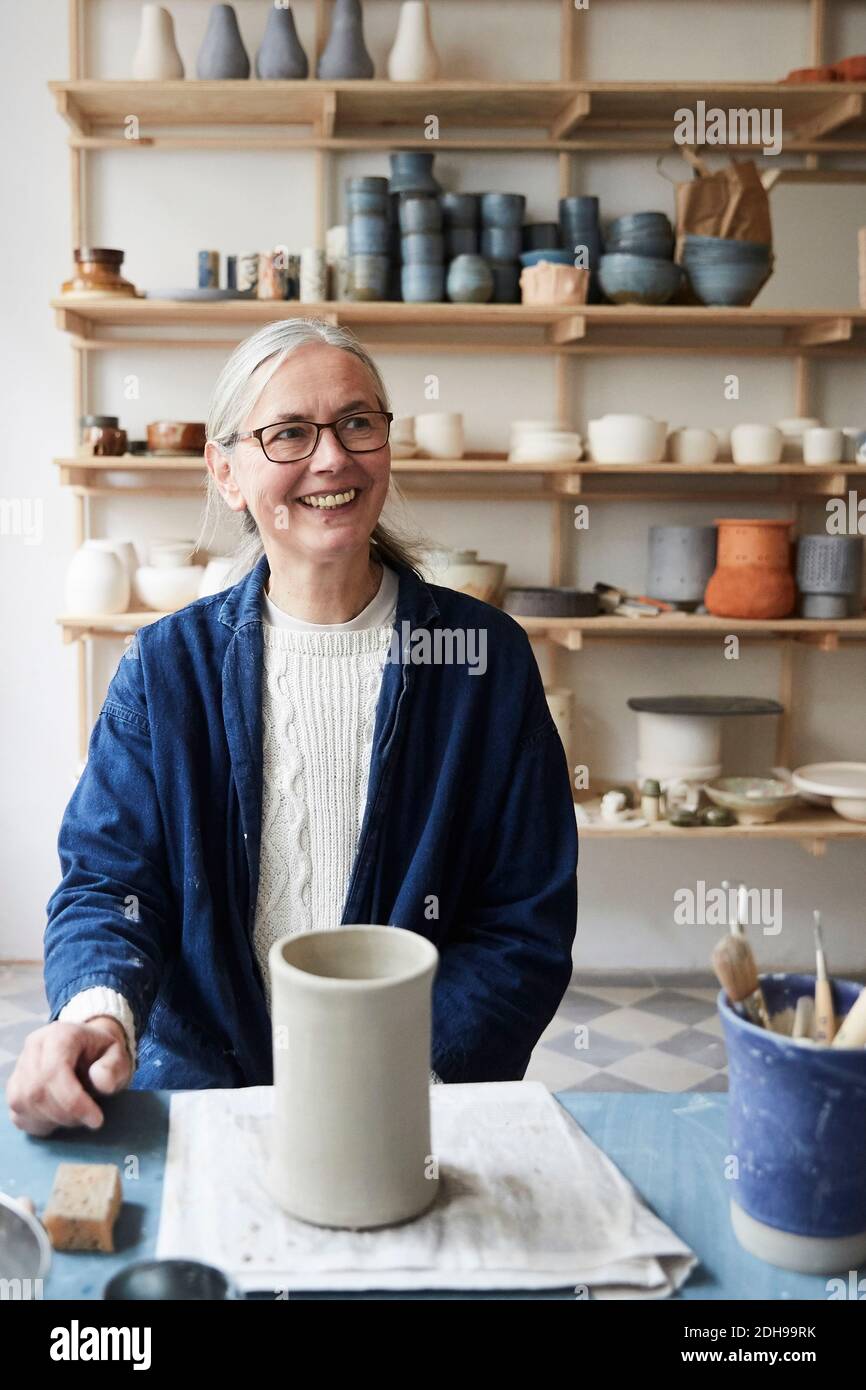 Smiling mature woman looking away while sitting at table in art class Stock Photo