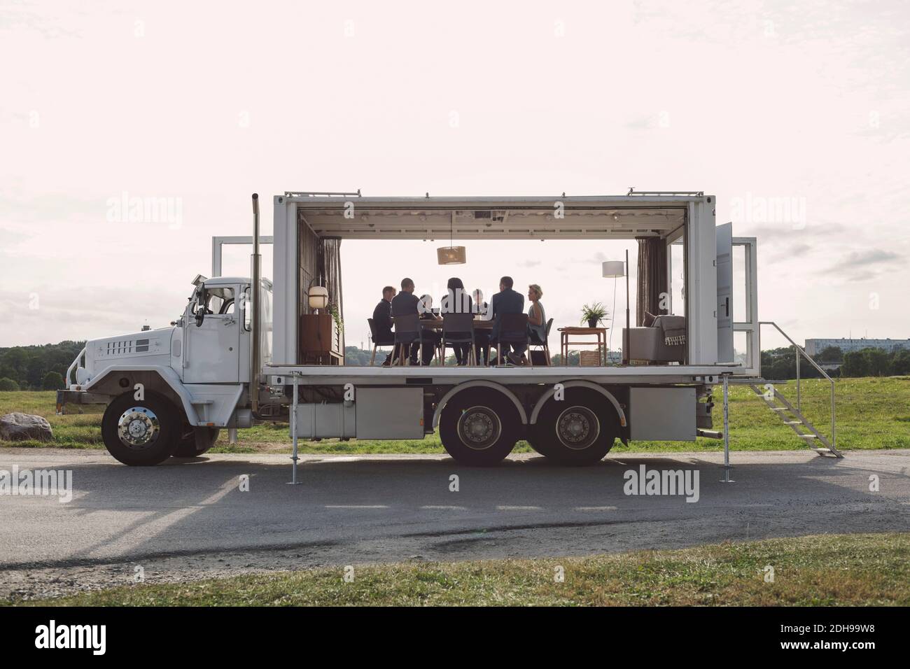 Business people discussing in portable office truck on road by field against sky Stock Photo