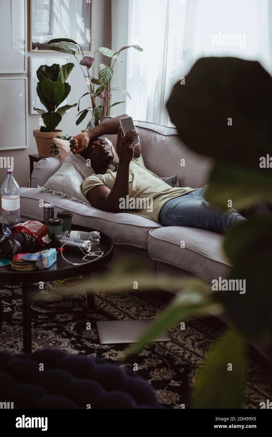 Sad man using smart phone while lying on sofa at home Stock Photo