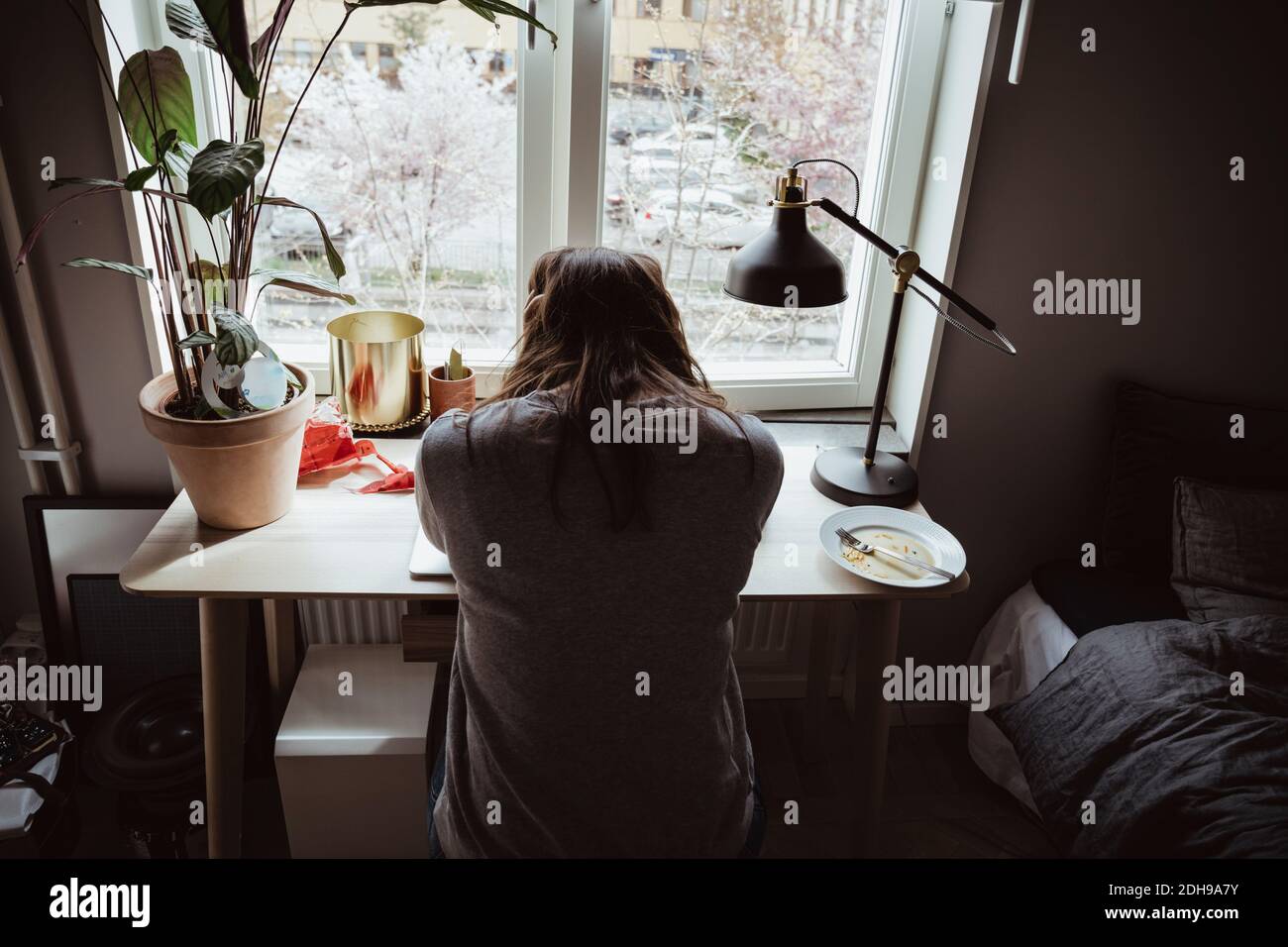 Rear view of worried woman sitting against window Stock Photo
