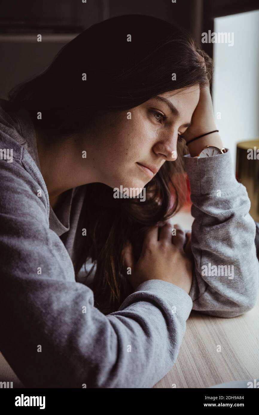 Sad woman looking away while sitting at table Stock Photo