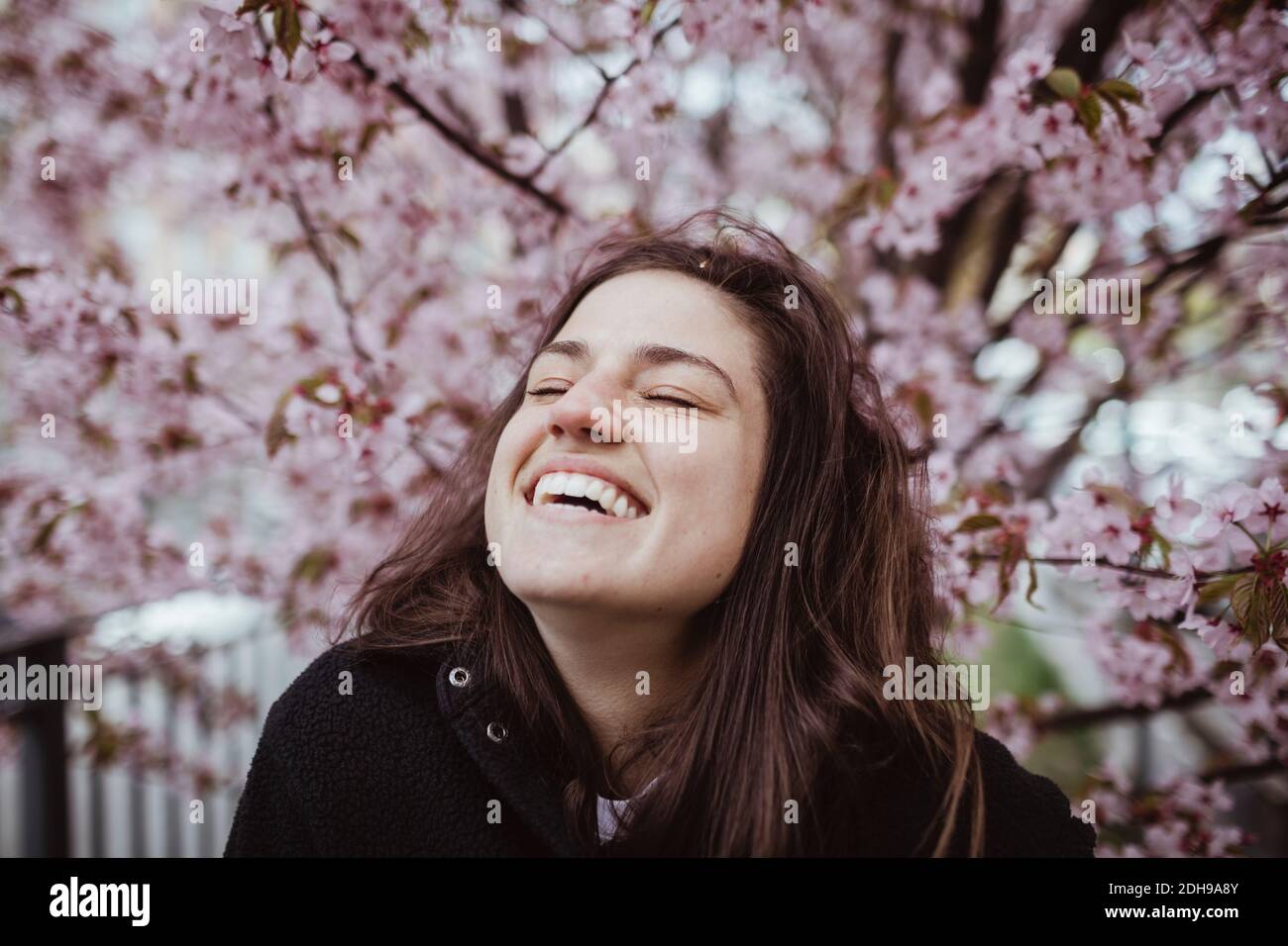 Happy woman with eyes closed standing against tree Stock Photo