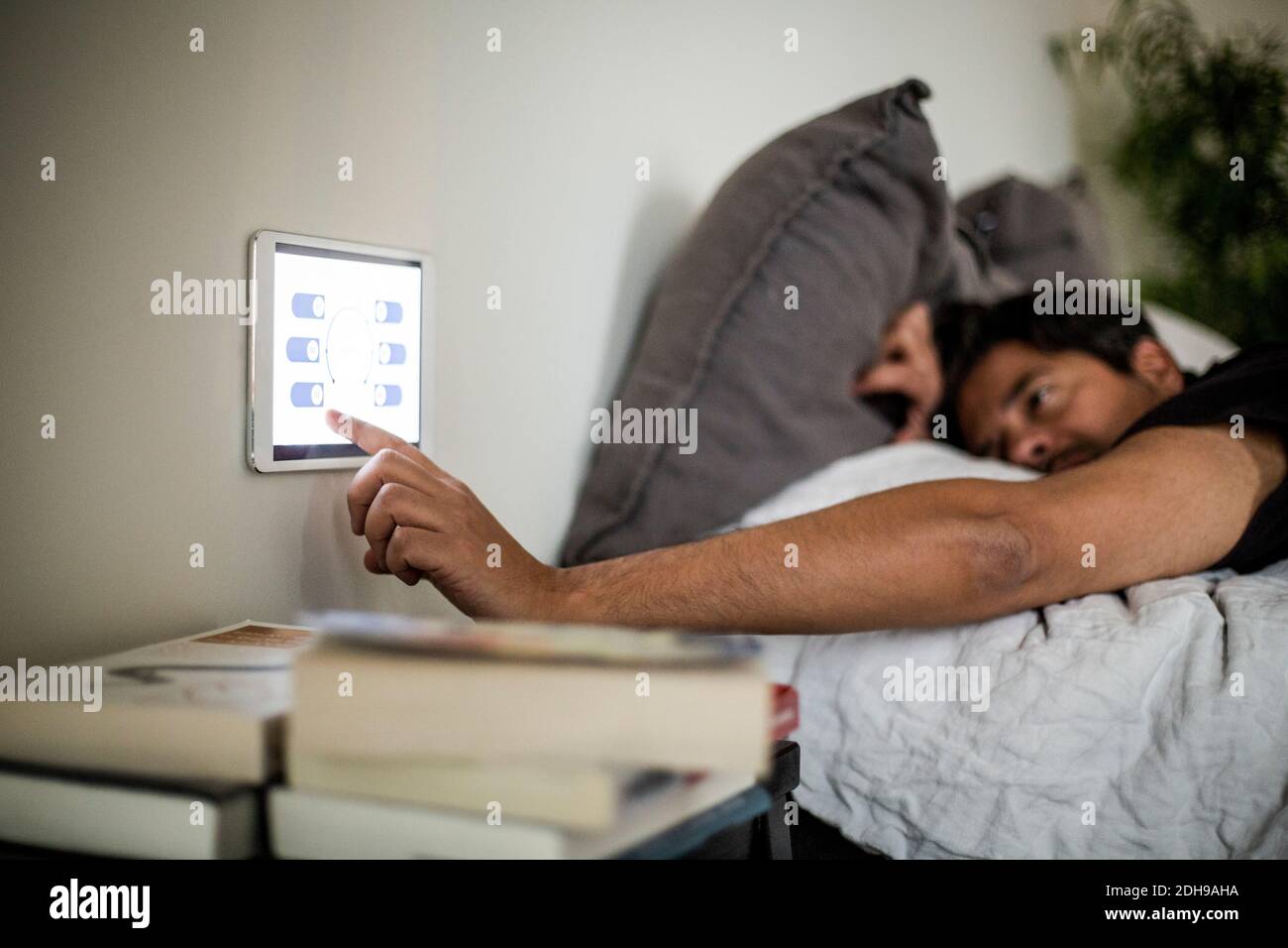 Man using digital tablet mounted on wall while lying on bed at smart home Stock Photo