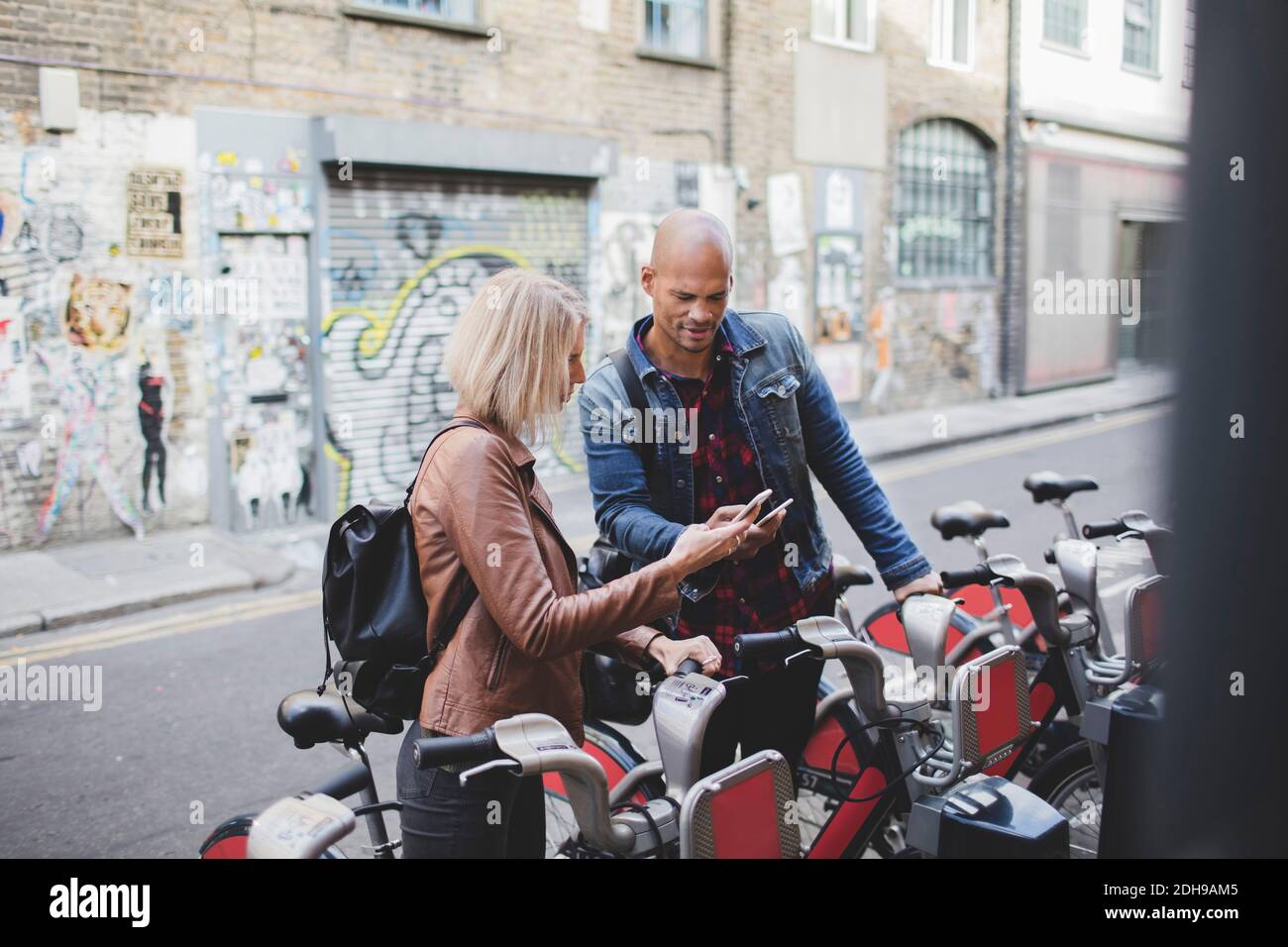 Couple using mobile phones at bicycle sharing system Stock Photo