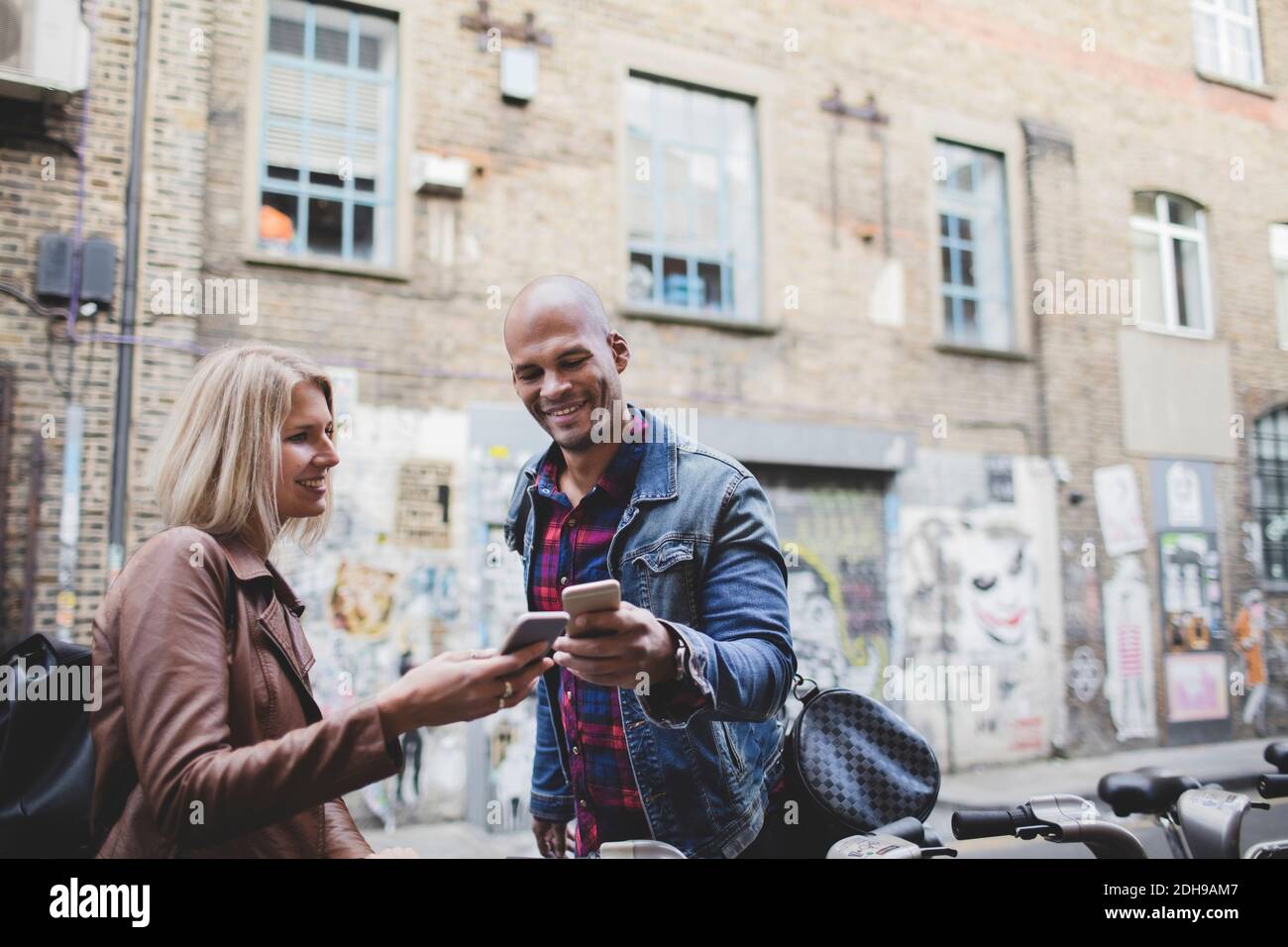 Multi-ethnic couple using mobile phones at bicycle sharing system Stock Photo