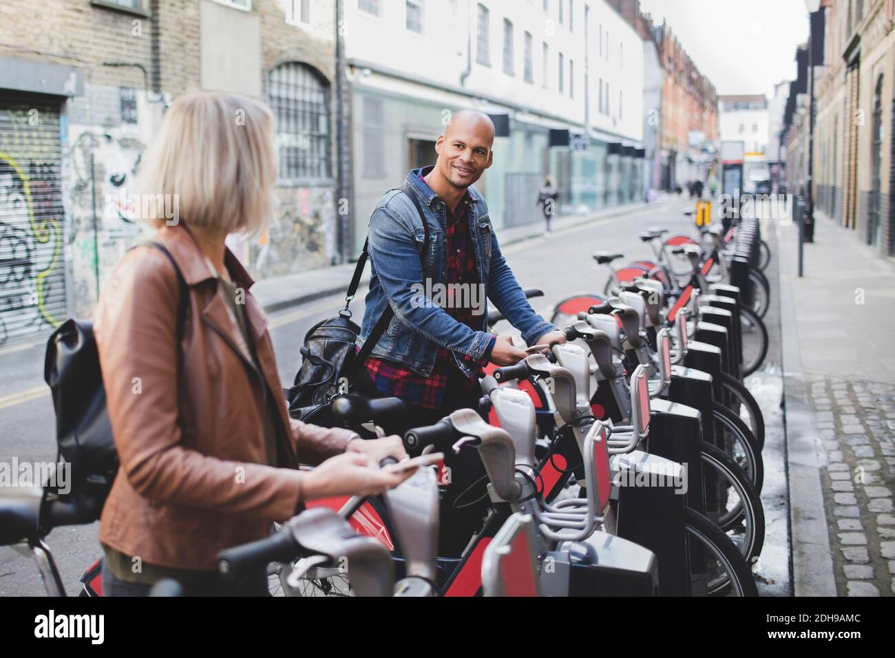 Multi-ethnic couple renting bicycles from bike share stand in city Stock Photo