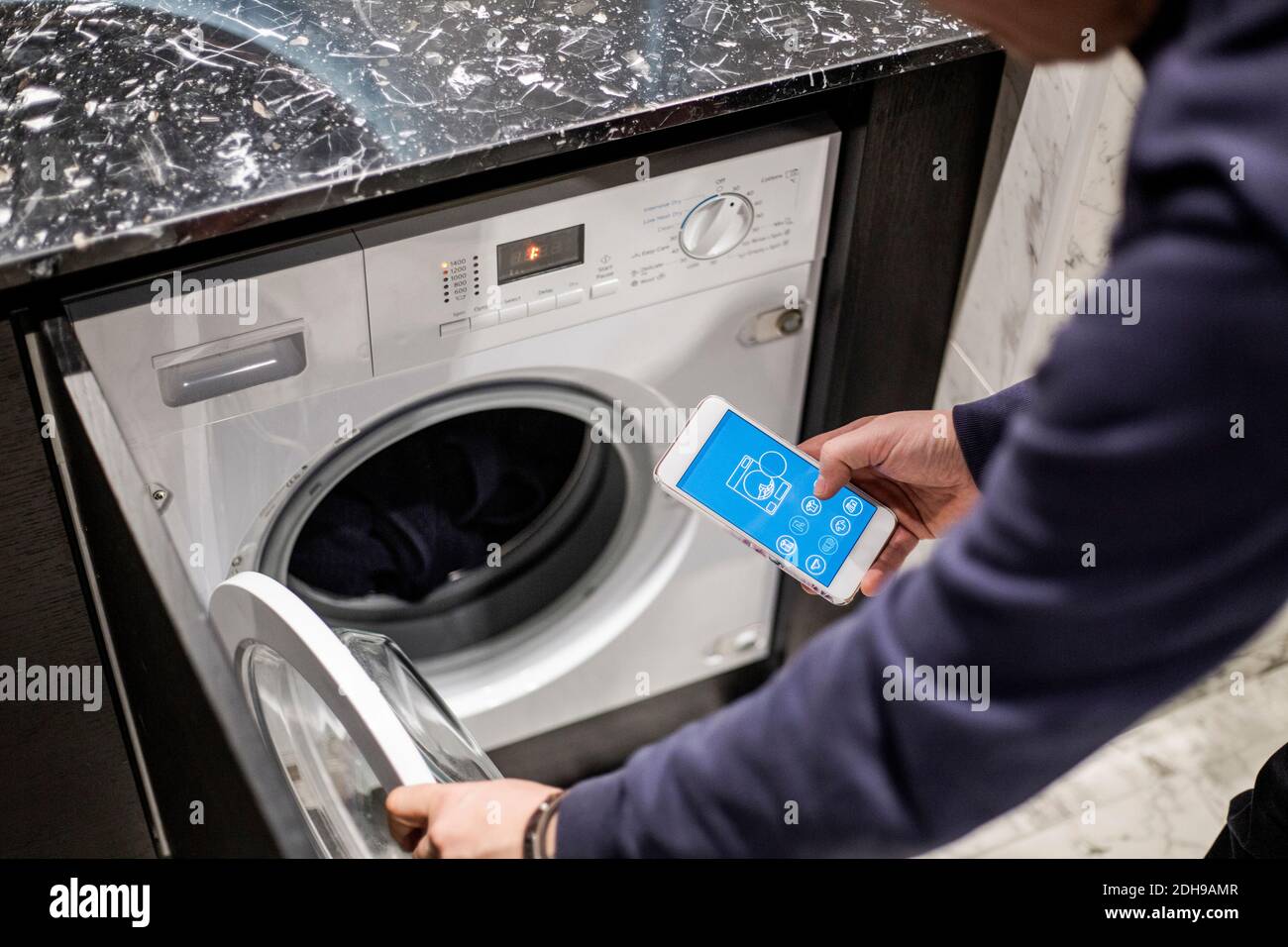 Cropped image of man controlling washing machine with mobile app at smart home Stock Photo
