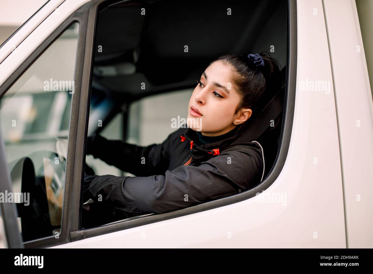 Young delivery woman looking through window while driving truck Stock Photo