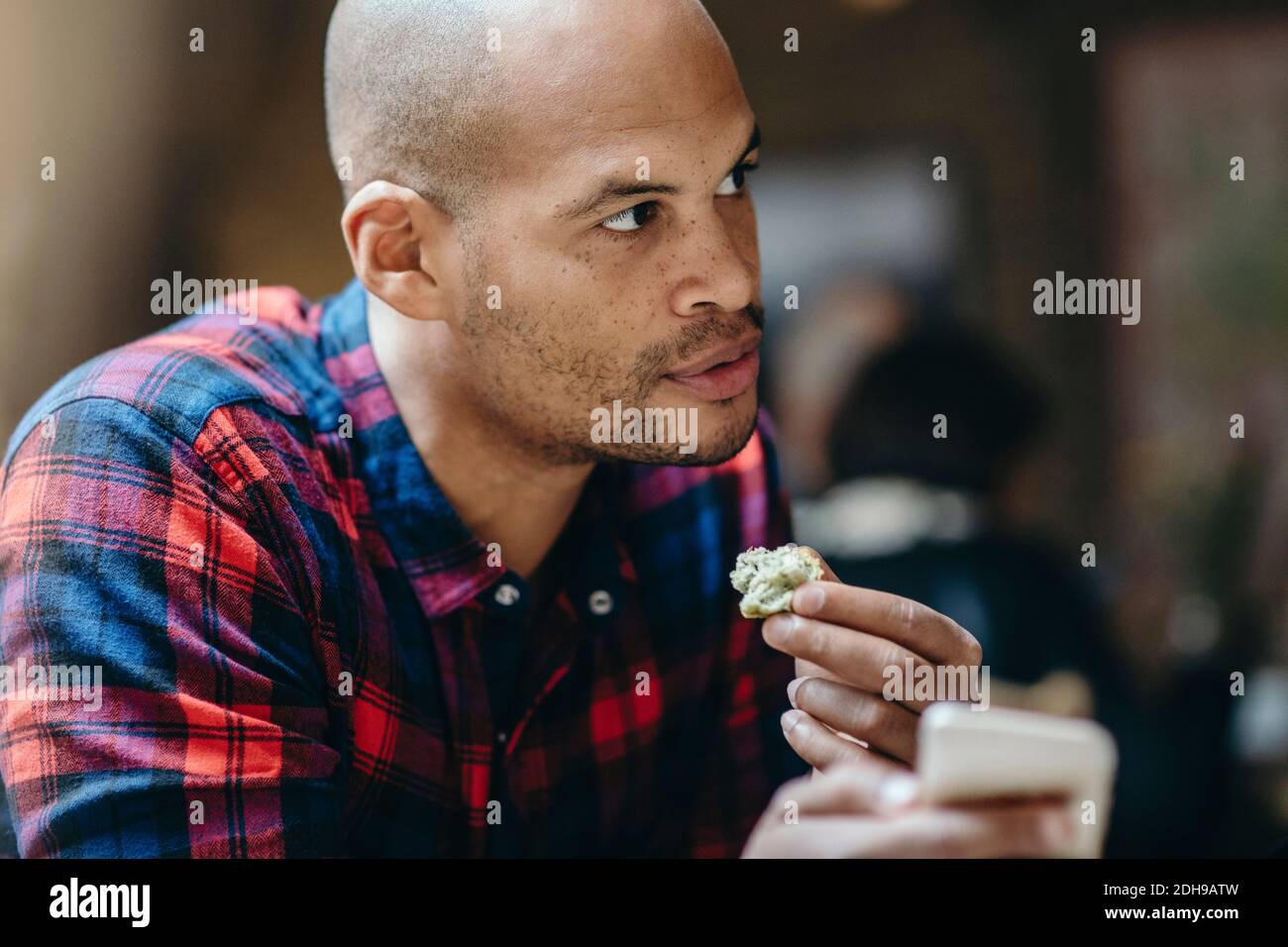 Mid adult man having food while holding mobile phone in coffee shop Stock Photo