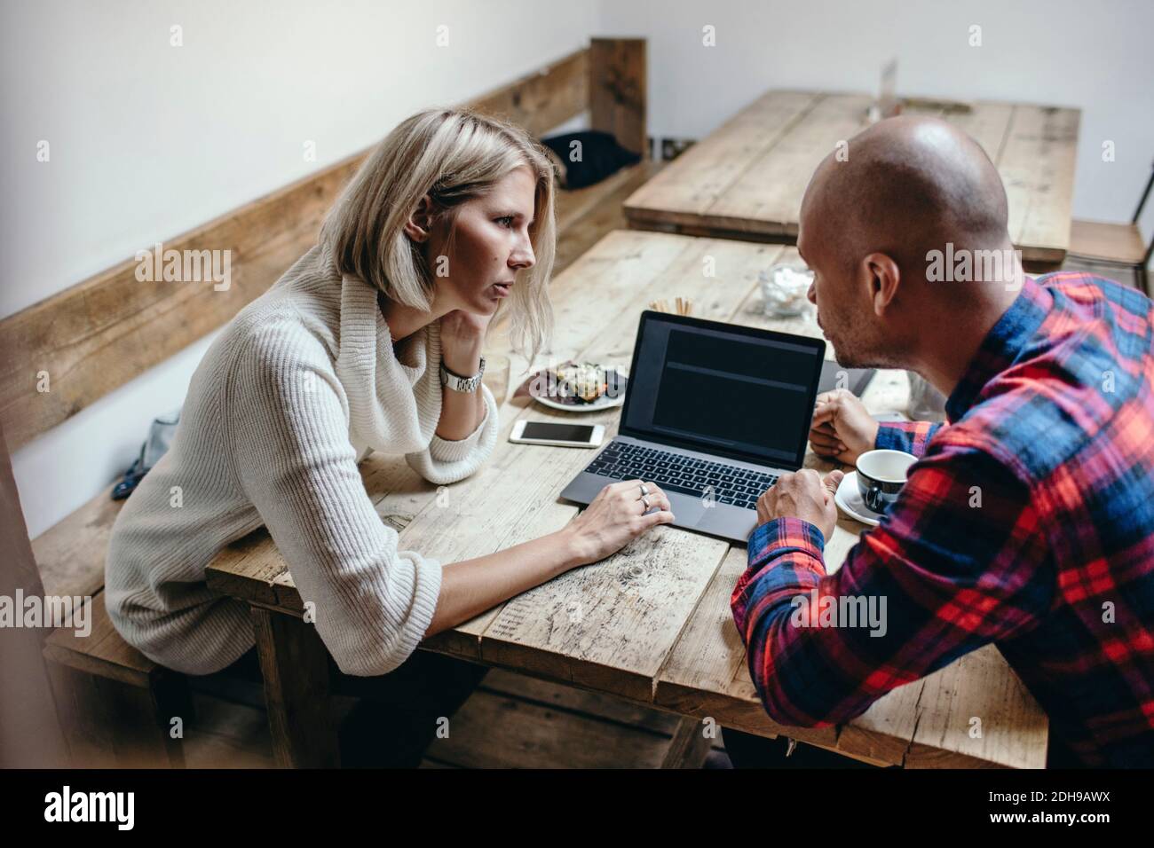 Multi-ethnic couple discussing while using laptop at table in coffee shop Stock Photo