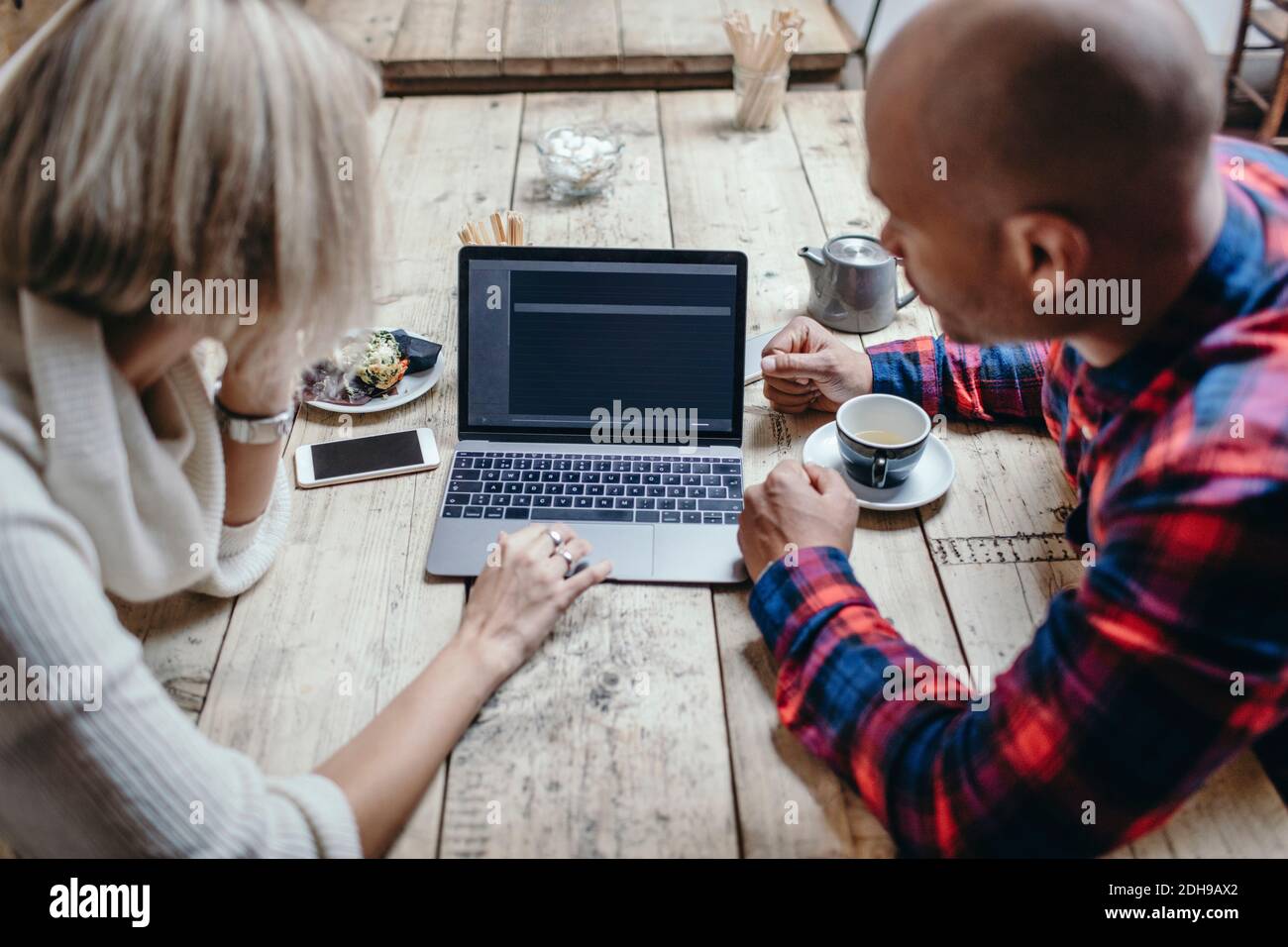 Multi-ethnic couple using laptop at table in coffee shop Stock Photo
