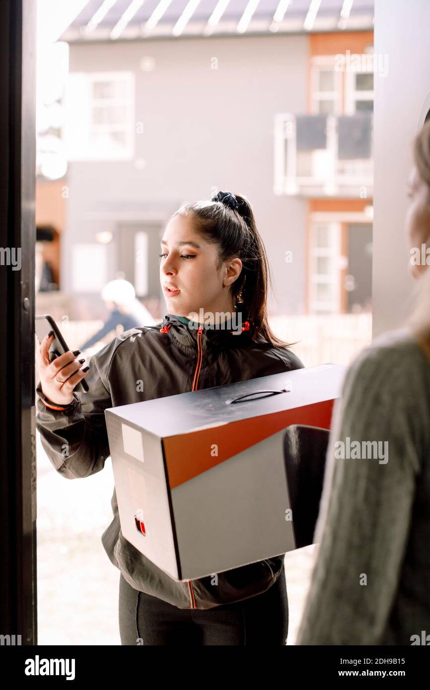 Delivery young woman using mobile phone while delivering package to customer Stock Photo
