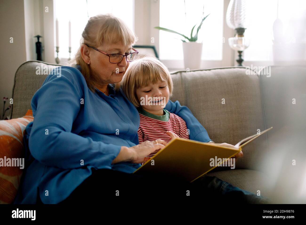 Grandmother reading storybook for grandson while sitting on sofa in living room Stock Photo