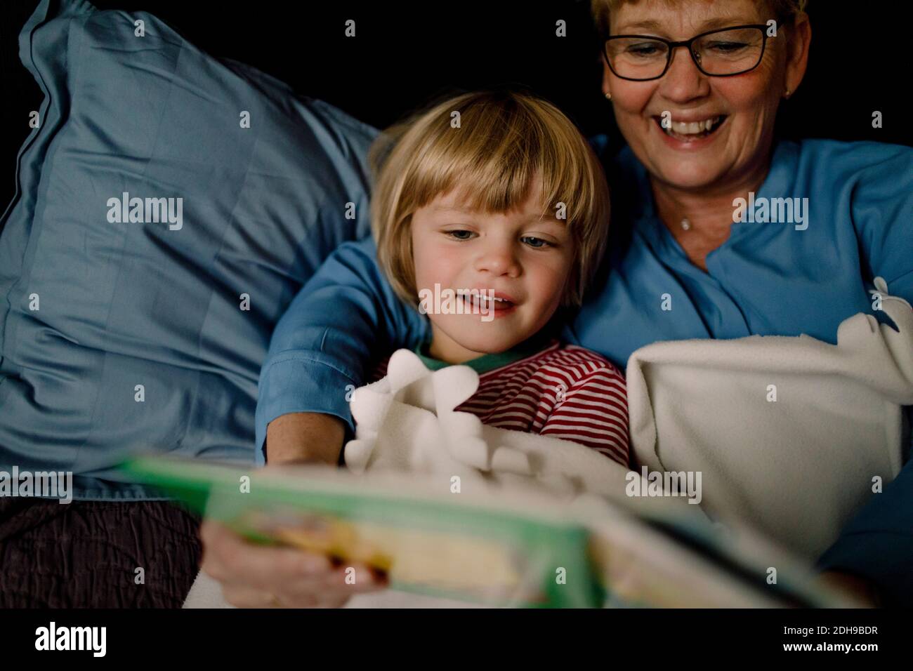 Smiling grandmother reading story book for grandson on bed at home Stock Photo