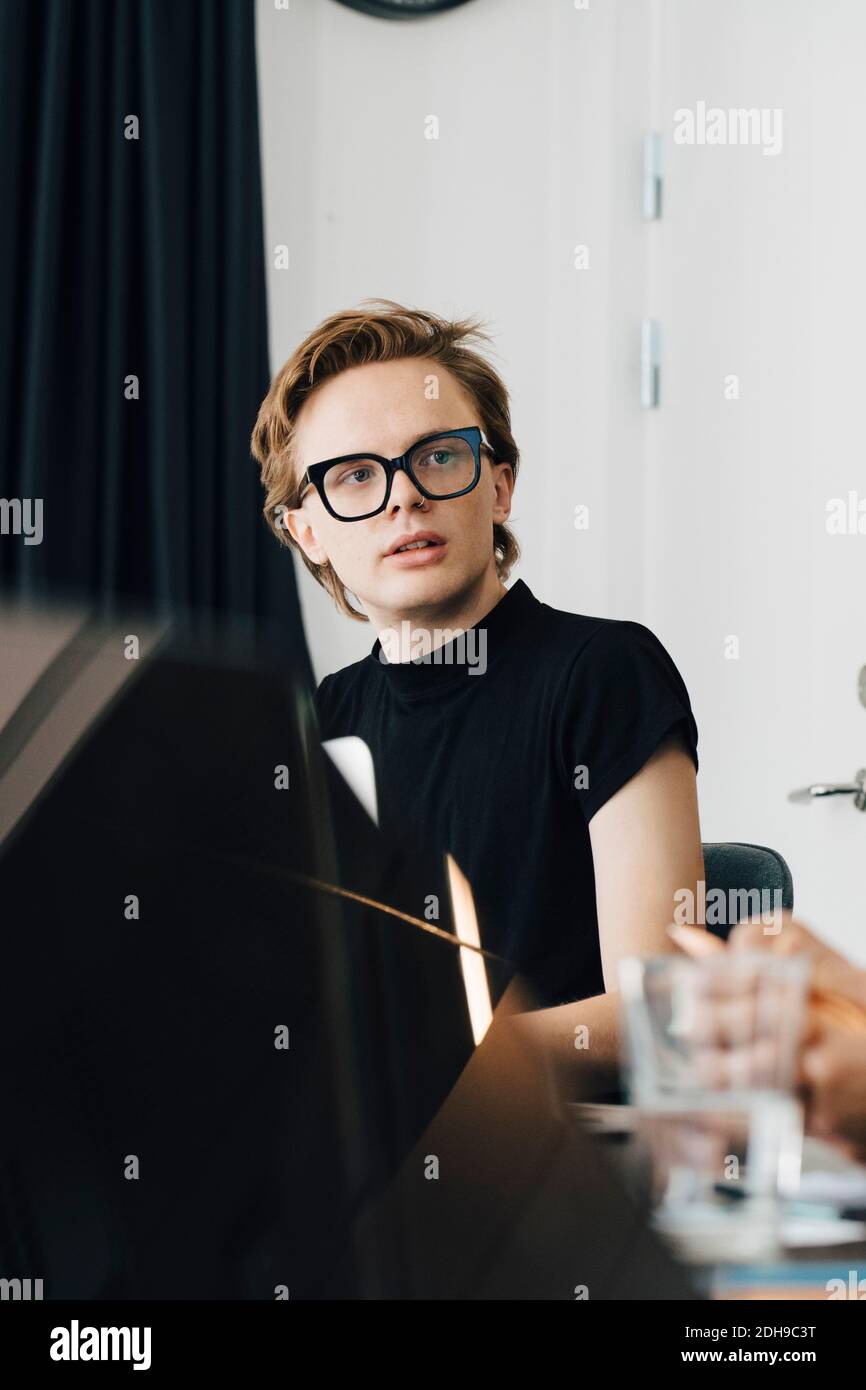 Young genderblend professional looking away while sitting in board room during meeting Stock Photo