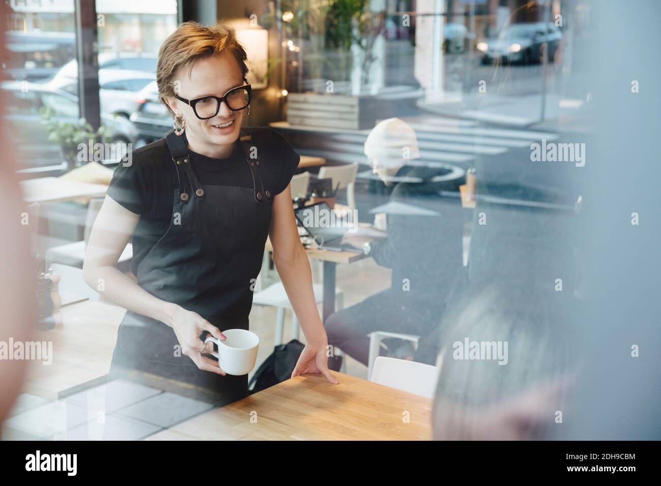 Smiling androgynous barista talking with customer in coffee shop Stock Photo