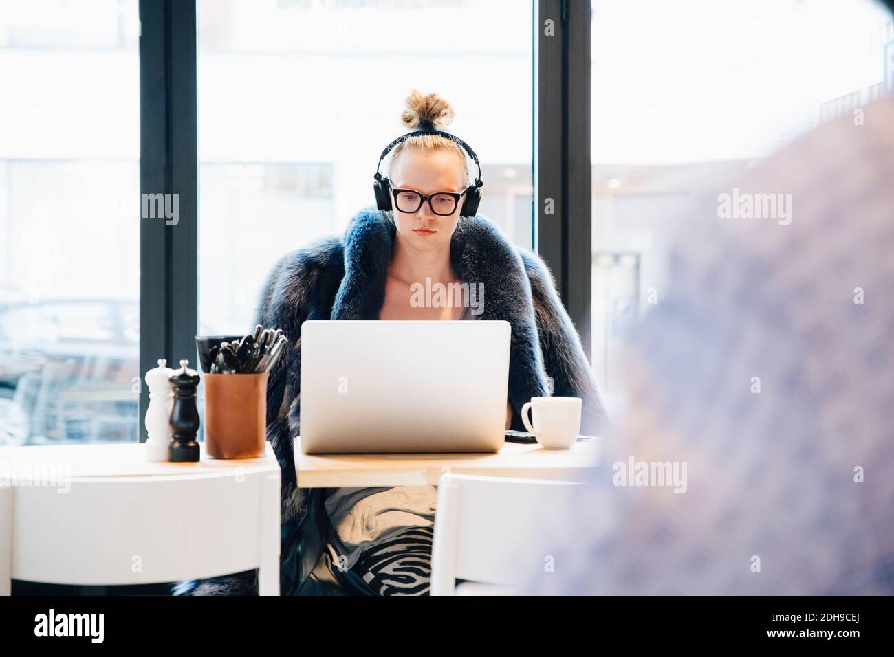 Confident young androgynous male customer using laptop against window at cafe Stock Photo