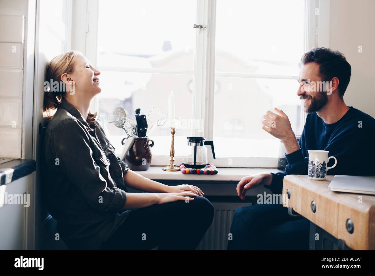 Happy couple sitting in kitchen against window at home Stock Photo