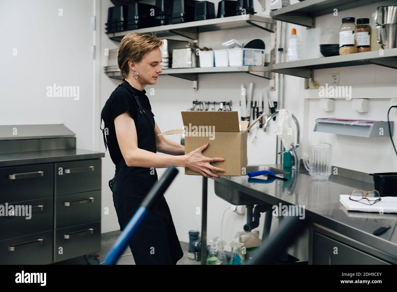 Side view of androgynous owner holding cardboard box in cafe kitchen Stock Photo