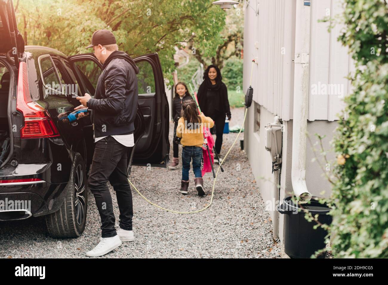 Man charging electric car while family loading luggage Stock Photo