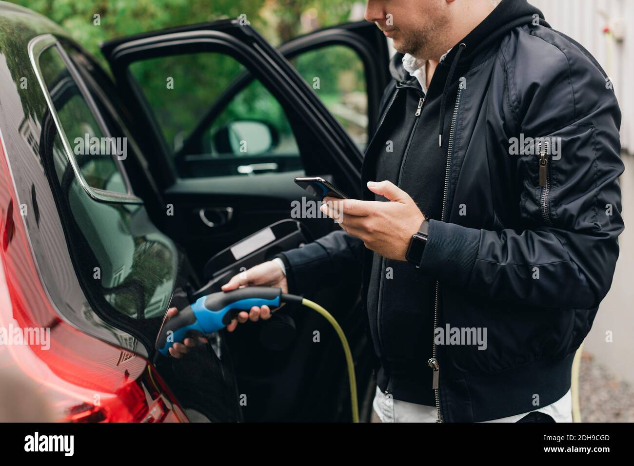 Mid adult man with electric car at charging station Stock Photo