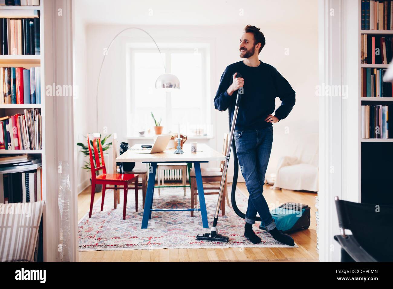 Happy man standing with vacuum cleaner in dining room at home Stock Photo