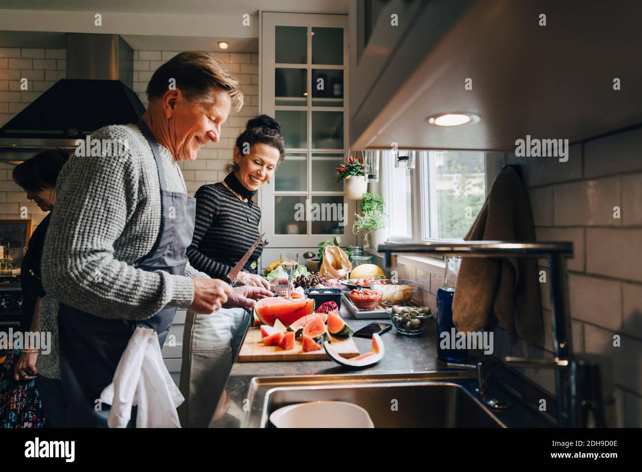 Smiling senior male and female friends cutting fruits at kitchen counter Stock Photo