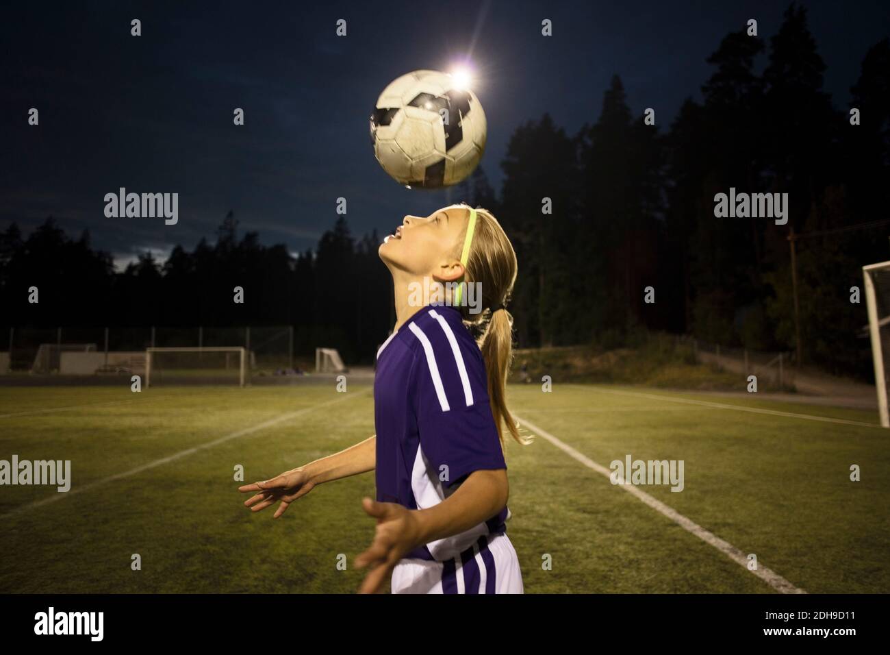 Side view of girl heading the ball on field against sky Stock Photo