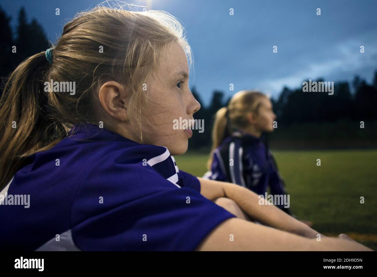 Side view of girl sitting at soccer field against sky Stock Photo