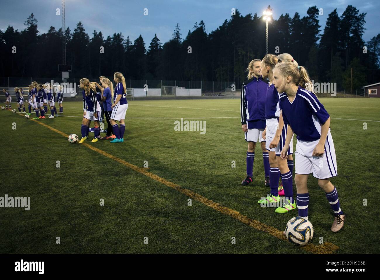 Girls standing with soccer balls on field Stock Photo