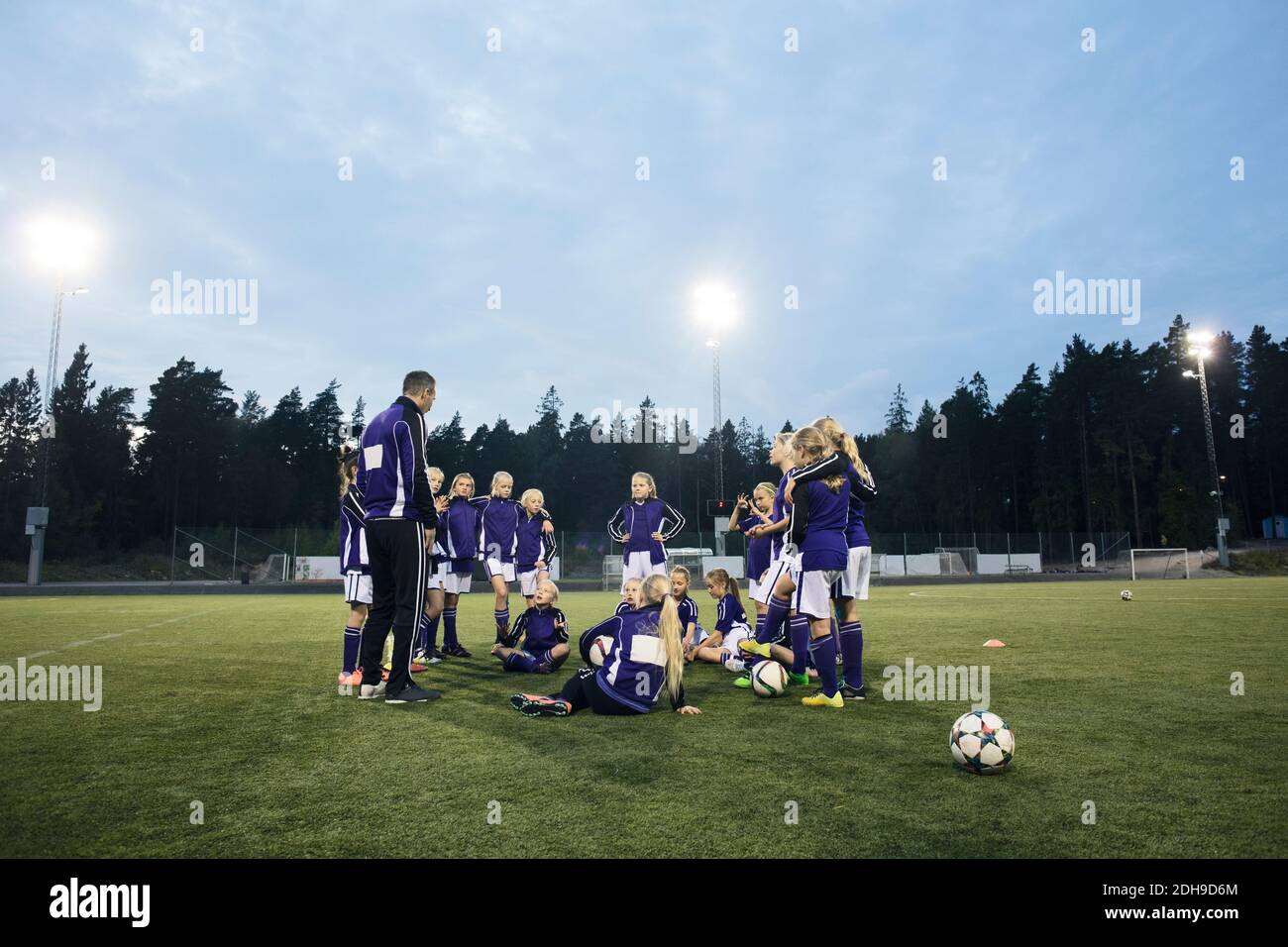 Coach standing by female soccer team on field against sky Stock Photo