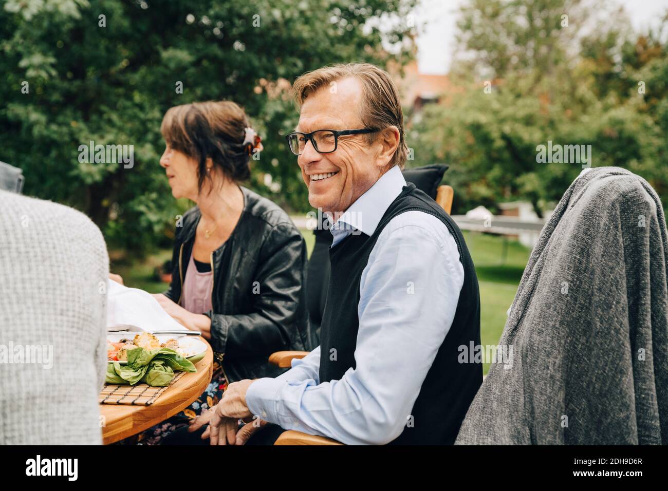 Smiling senior man sitting with friends at dining table in back yard Stock Photo