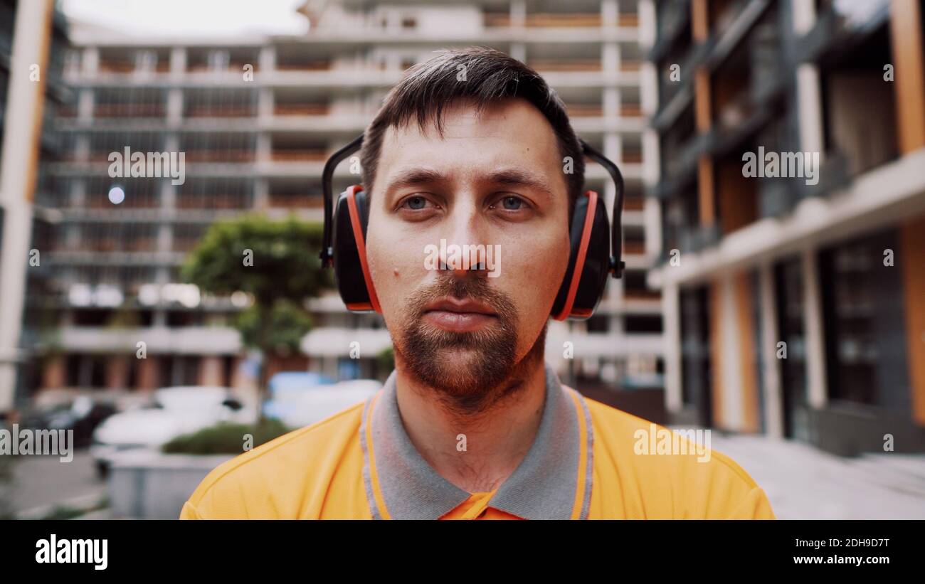 Construction worker with ear muff working at construction site. Worker puts on ear defenders to protect against sound. Taking ca Stock Photo