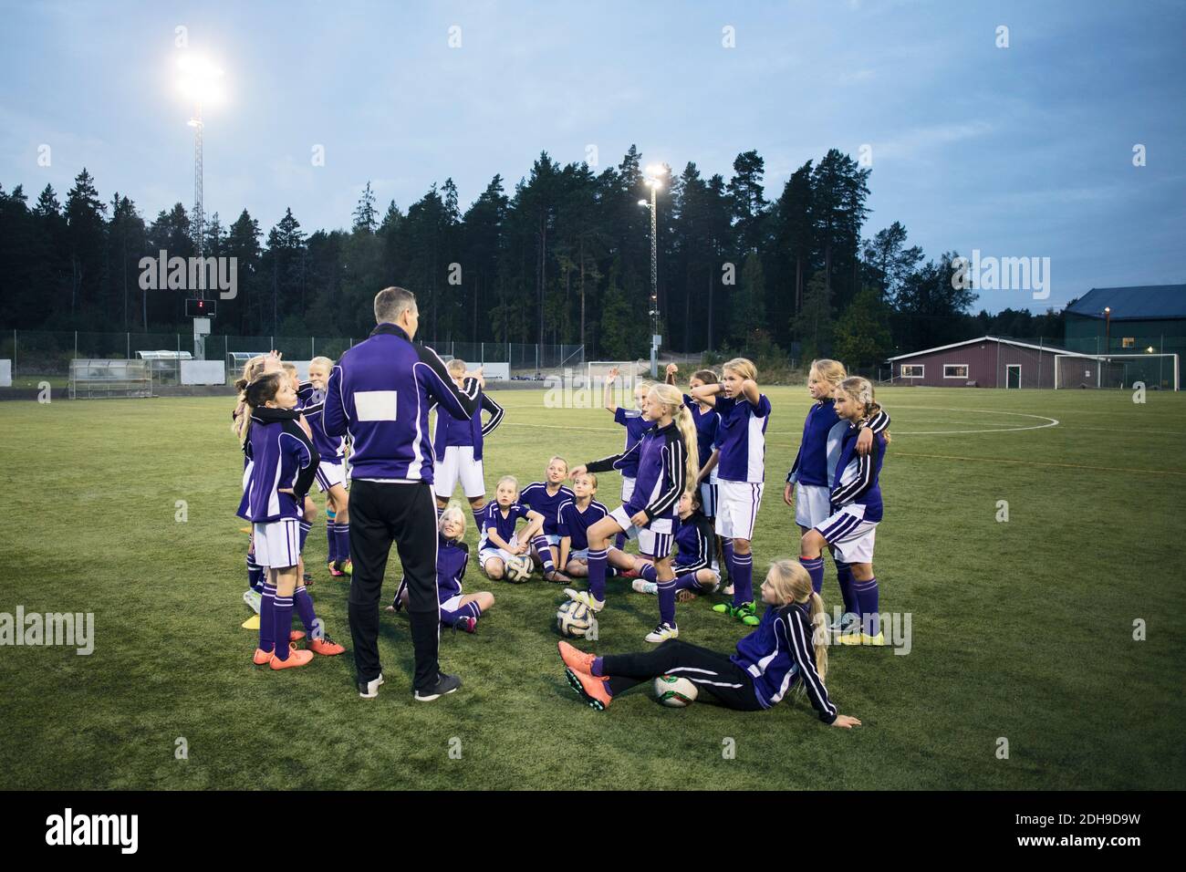 Coach explaining with girls soccer team on field against sky Stock Photo